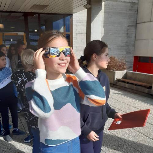 Schülerin schaut mit einer besonderen Brille in die Sonne um eine Sonnenfinsternis zu beobachten. 