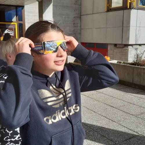 Schülerin schaut mit einer besonderen Brille in die Sonne um eine Sonnenfinsternis zu beobachten. 