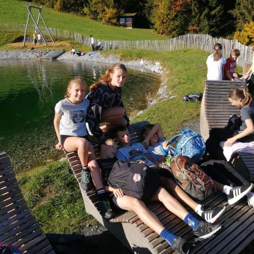Kinder spielen vor einem Teich auf Holzbänken