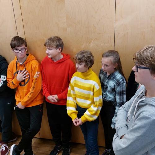 Schülerinnen und Schüler hören Aufmerksam zu, lehnen an der Wand.