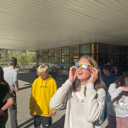 Schülerin schaut mit einer besonderen Brille in die Sonne um eine Sonnenfinsternis zu beobachten. 