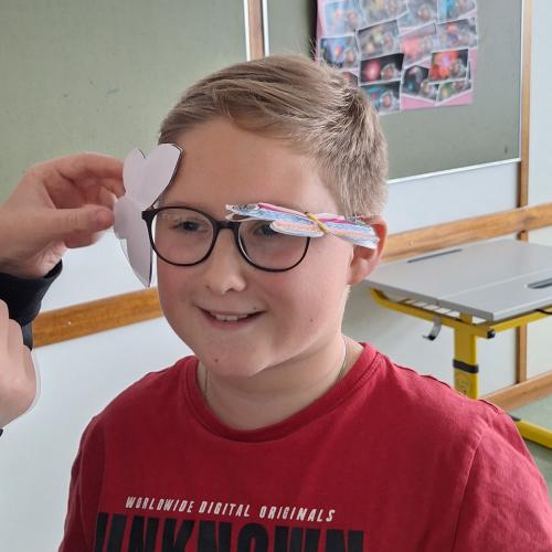 Selbstgebastelter Schmetterling wird im Schwerpunkt auf einem Brillenrahmen balanciert.