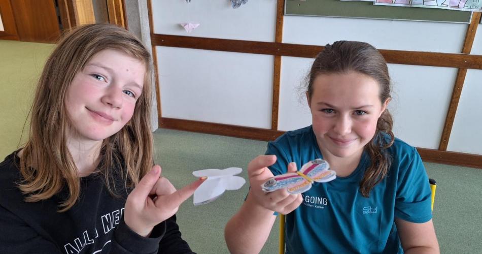 Zwei Schülerinnen balancieren selbst gebastelte Schmetterlinge  auf ihren Fingern.