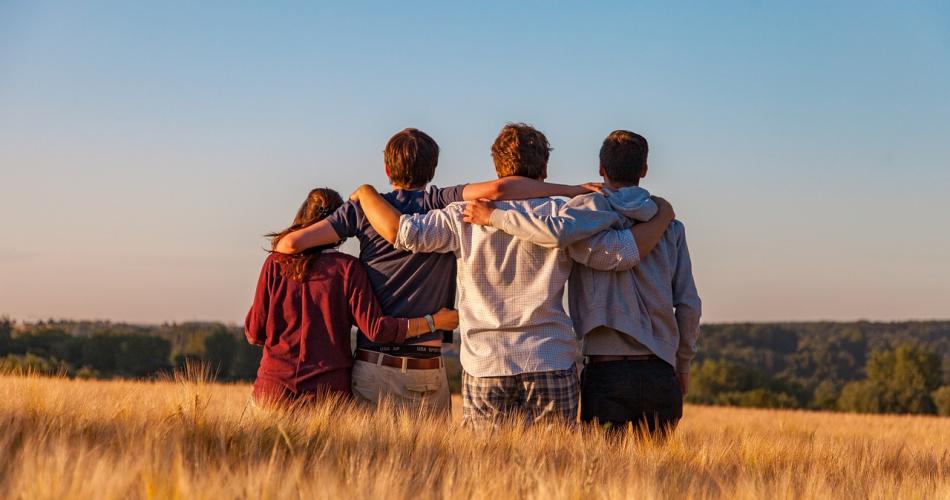 Freundesgruppe steht mit dem Rücken zum Fotografen in einem Kornfeld und legt die Arme um die Schultern des jeweils Nächsten.